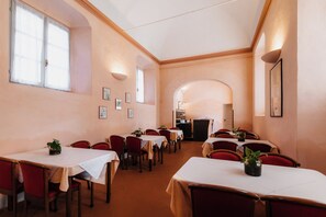 A dining area with tables and chairs, a kitchen in the background, and framed pictures on the walls. - Casa Regina Montis Regalis (Vicoforte)