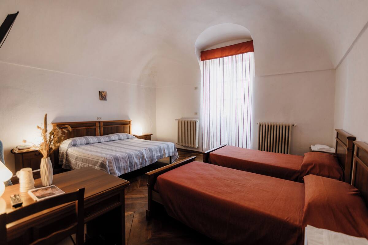 A room with a bed, a desk, and a chair. There is a window with curtains.