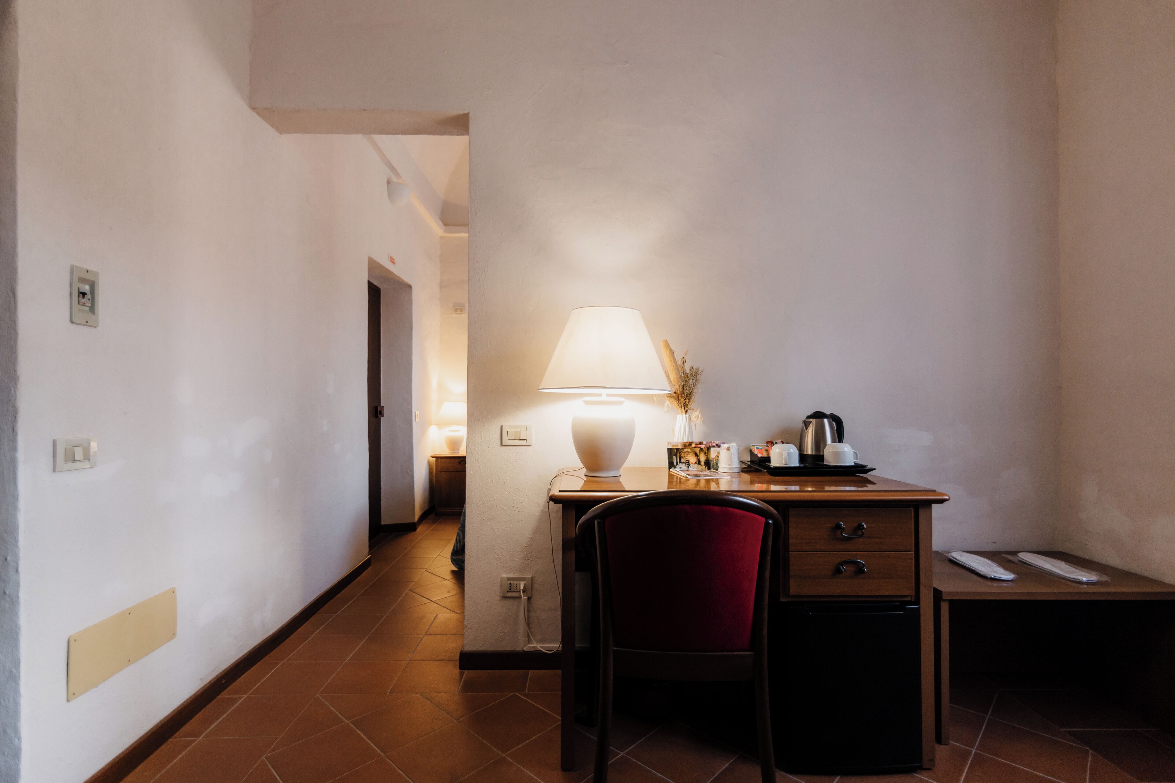 A small, well-lit room with a desk, chair, and a lamp.