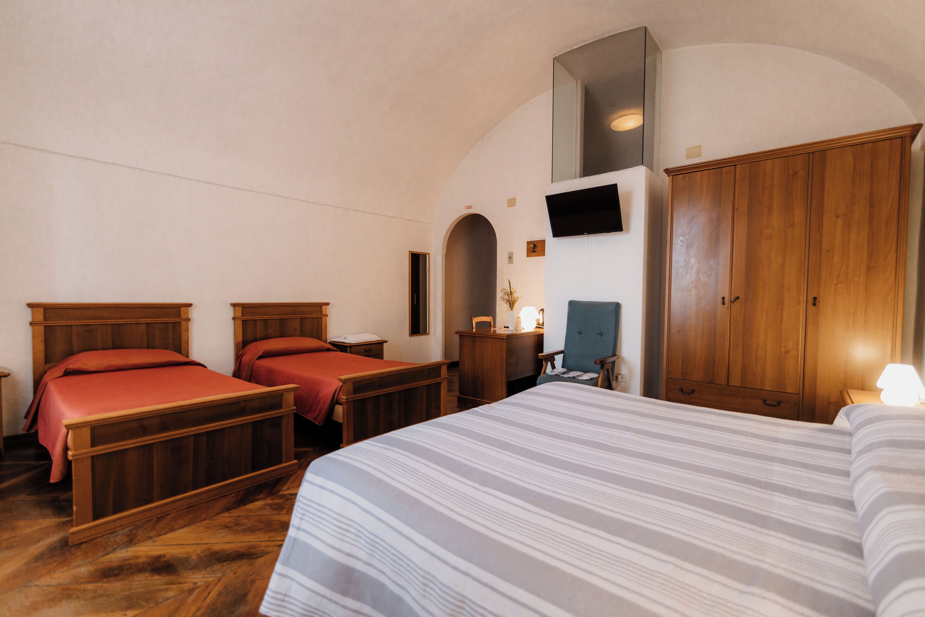 A bedroom with two wooden beds, a large wardrobe, and a television mounted on the wall.