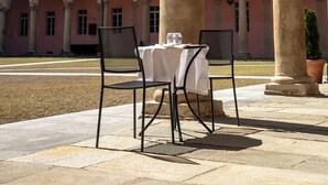 Une terrasse extérieure avec une table et des chaises, un bâtiment en briques orné d’arches et, au fond, un dôme.
