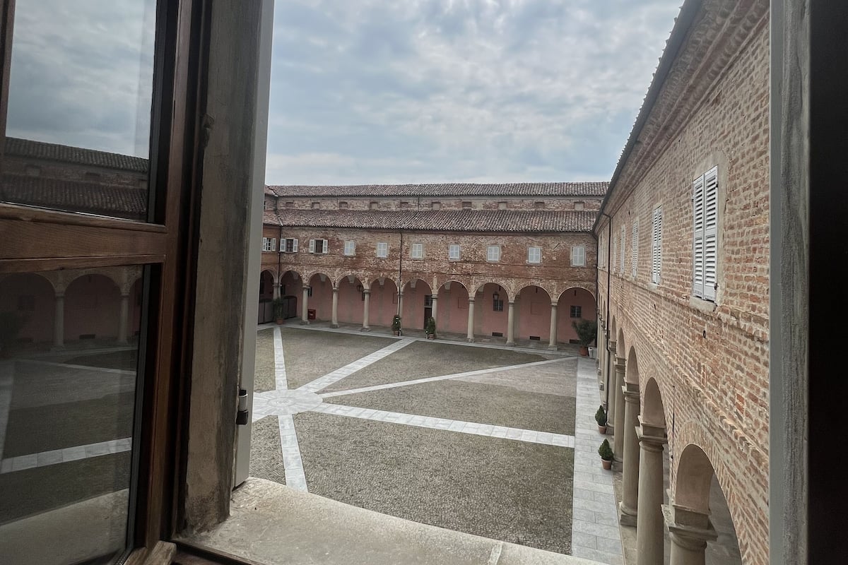 A courtyard with a brick building, arched walkways, and a view through a window.