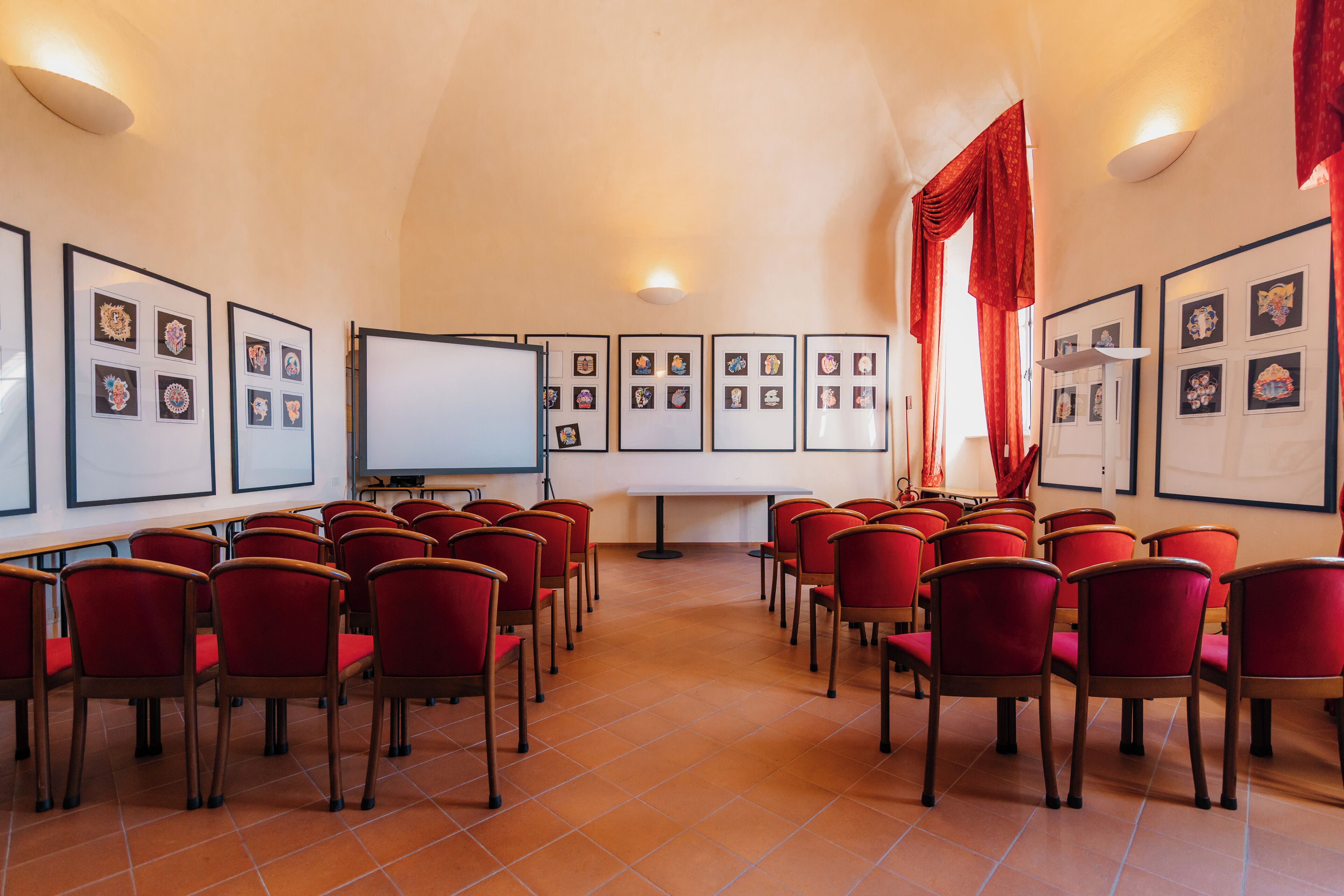 A conference room with red chairs arranged in rows, a whiteboard, and framed pictures on the walls.