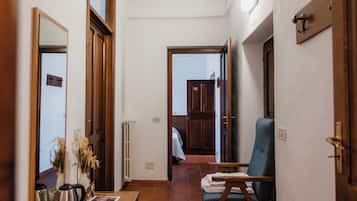 A hallway with a wooden bench, a chair, and a small table with a vase and a kettle.