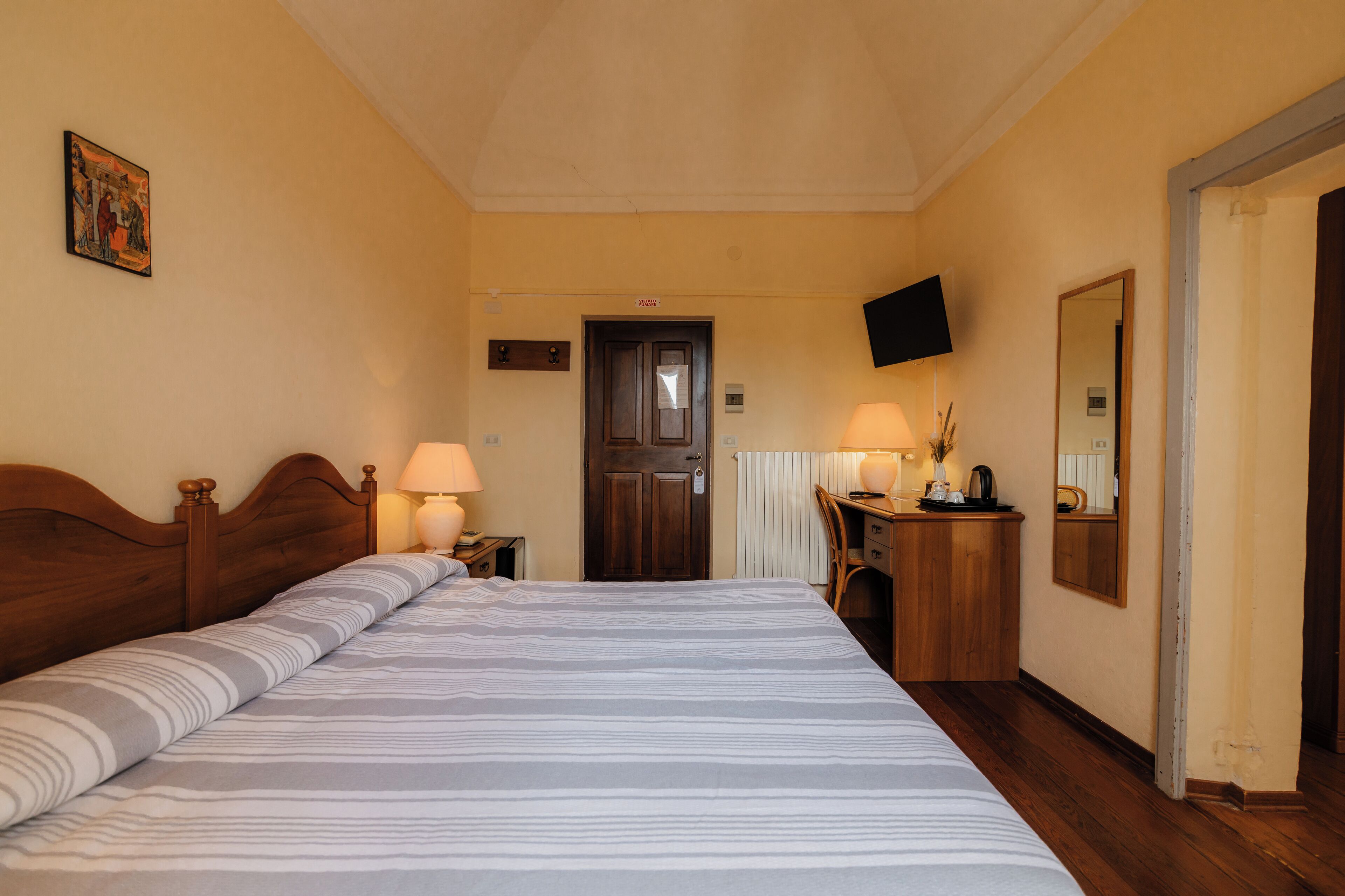 Habitación de hotel con una cama grande, dos lámparas de noche, un escritorio de madera con lámpara, un espejo y un televisor en la pared.