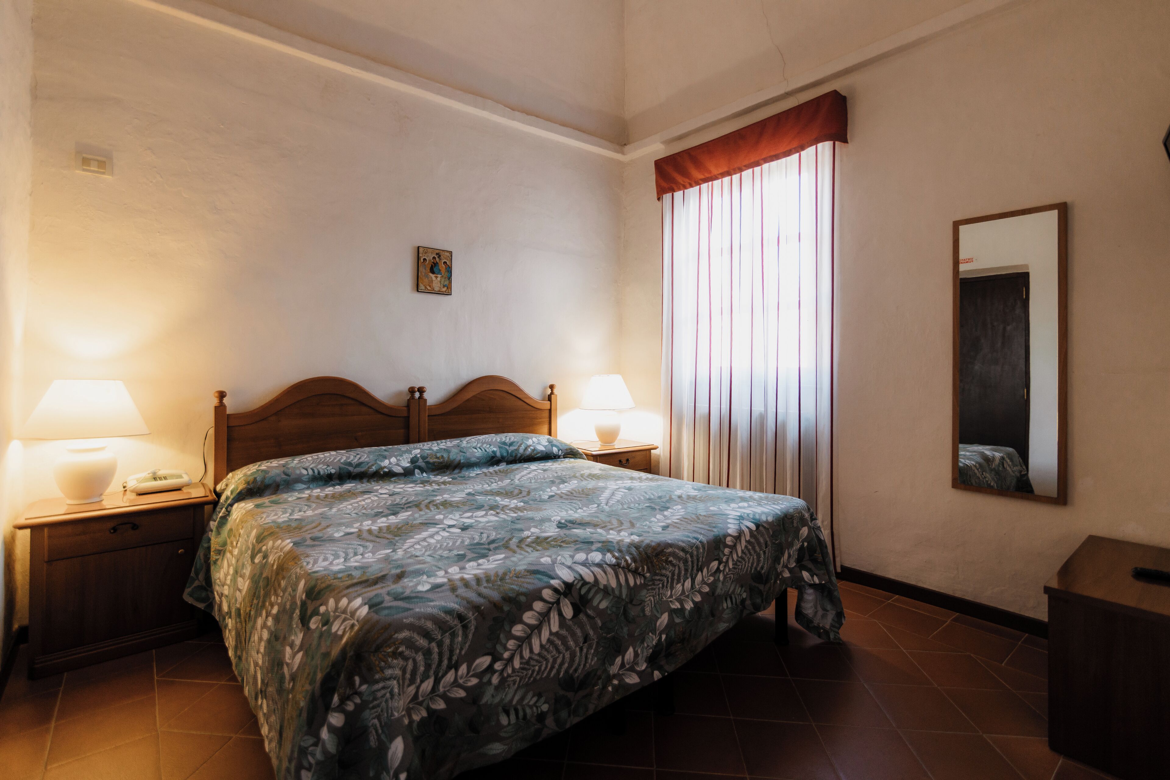 Een slaapkamer met een bed, twee nachtkastjes, een spiegel en een raam met gordijnen.