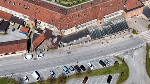 Vue aérienne d’un bâtiment historique doté d’un dôme imposant, entouré de champs verdoyants et d’un parking.