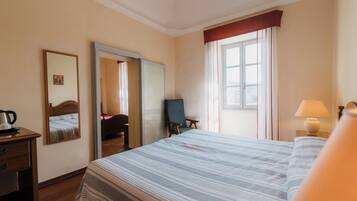 Ein Hotelzimmer mit einem Bett, einem Schreibtisch mit Lampe, einem Stuhl, einem Spiegel und einem Fenster mit Vorhängen.