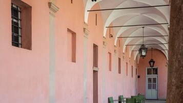 Un corridoio con sedie verdi disposte lungo le pareti, un pavimento in pietra e una serie di archi con lanterne sospese.