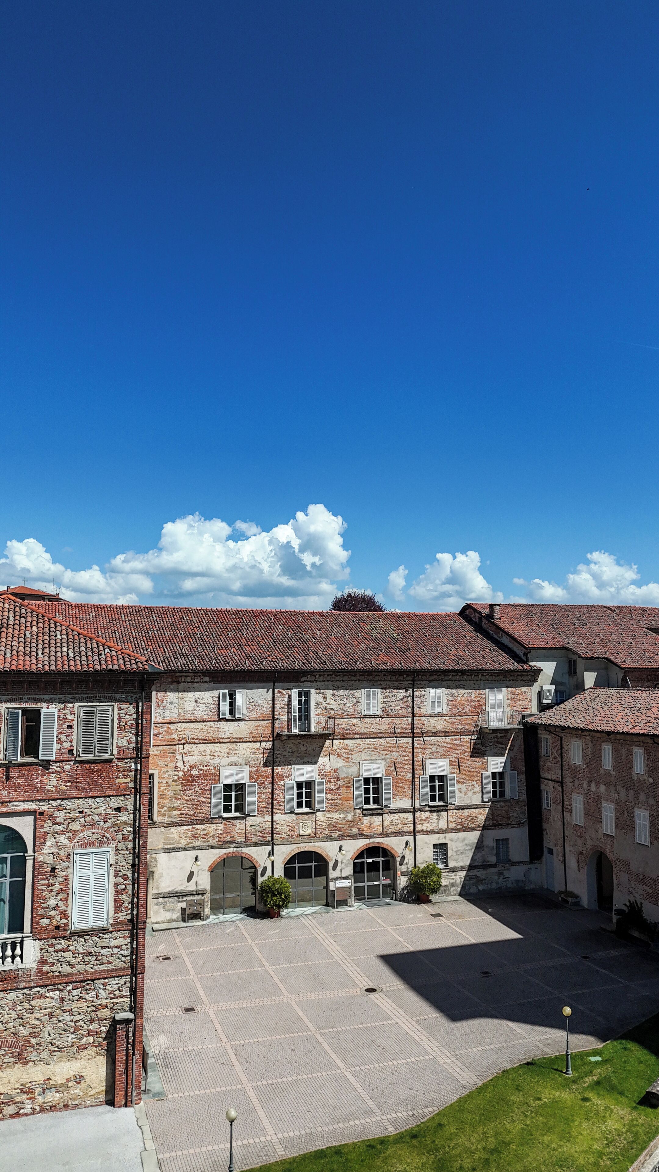 A courtyard with a building featuring a red-tiled roof, multiple windows, and a paved area.