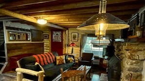 Interior acollidor d'una cabana, amb un sofà de fusta, una taula escocesa i una llar de pedra.