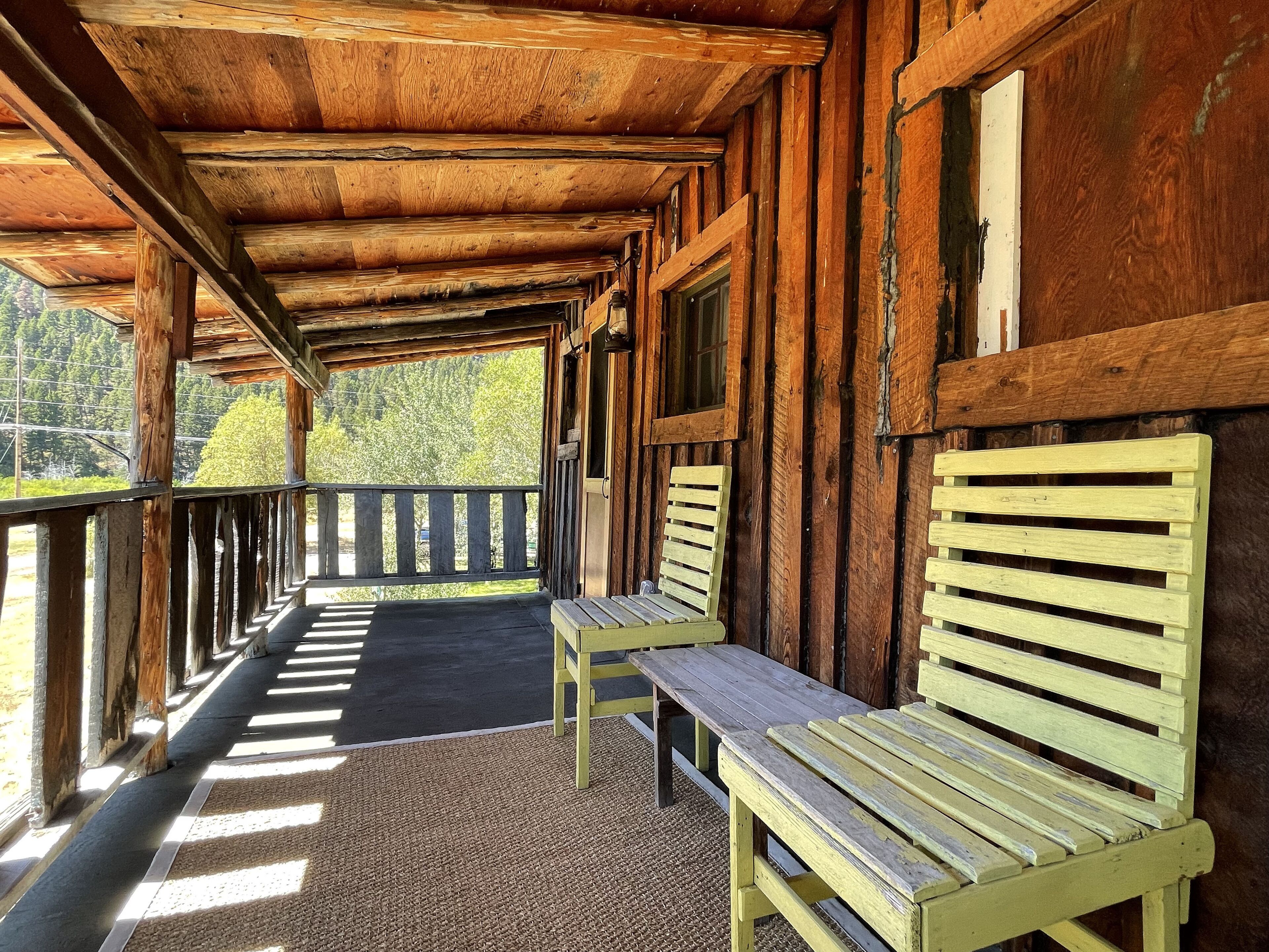 Une cabane en bois dotée d’un porche couvert, de deux bancs en bois et offrant une vue sur les arbres.