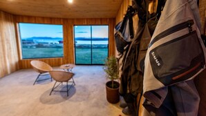 A room with a large window overlooking a body of water, a chair, a small table, and a coat rack with a jacket. - The Line Hotel (Natales)