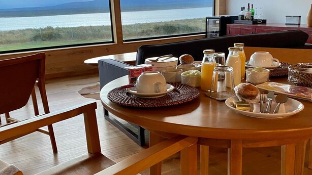 A dining area with a table set for breakfast, overlooking a scenic view of the sea and mountains. - The Line Hotel (Natales)