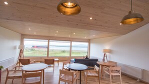 A spacious room with wooden flooring, a round table, and several chairs. There is a large window offering a view of the outdoors. - The Line Hotel (Natales)