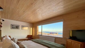 A bedroom with a large bed, a television, a window with a view, and wooden ceiling. - The Line Hotel (Natales)