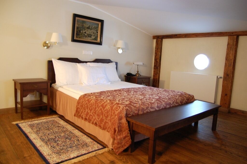 A bedroom with a bed, bedside tables, a nightstand, a bench, a rug, and a wall-mounted lamp.