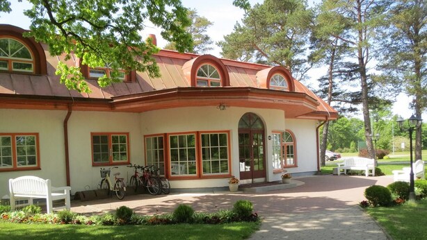 A two-story building with a curved roof, large windows, and a paved entrance.