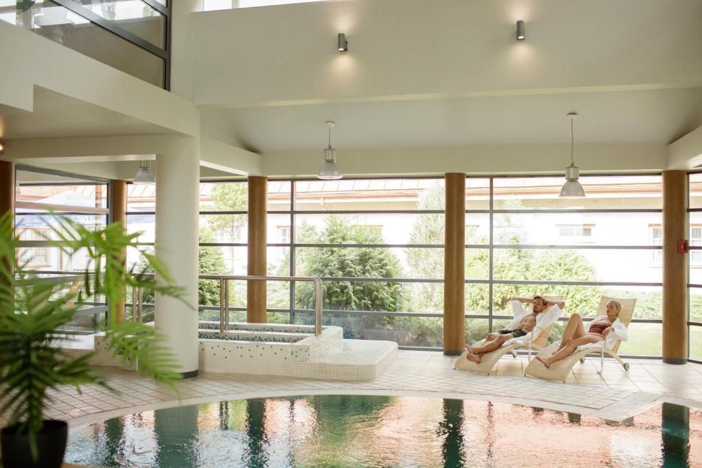 Piscina interna com vista para o exterior, cadeiras de descanso e um elemento aquático.