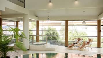 Piscina interna com vista para o exterior, cadeiras de descanso e um elemento aquático.