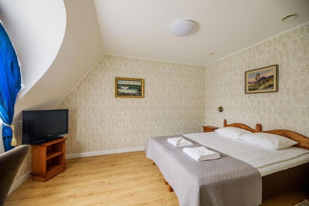 A bedroom with a bed, a television on a stand, and two framed pictures on the wall.