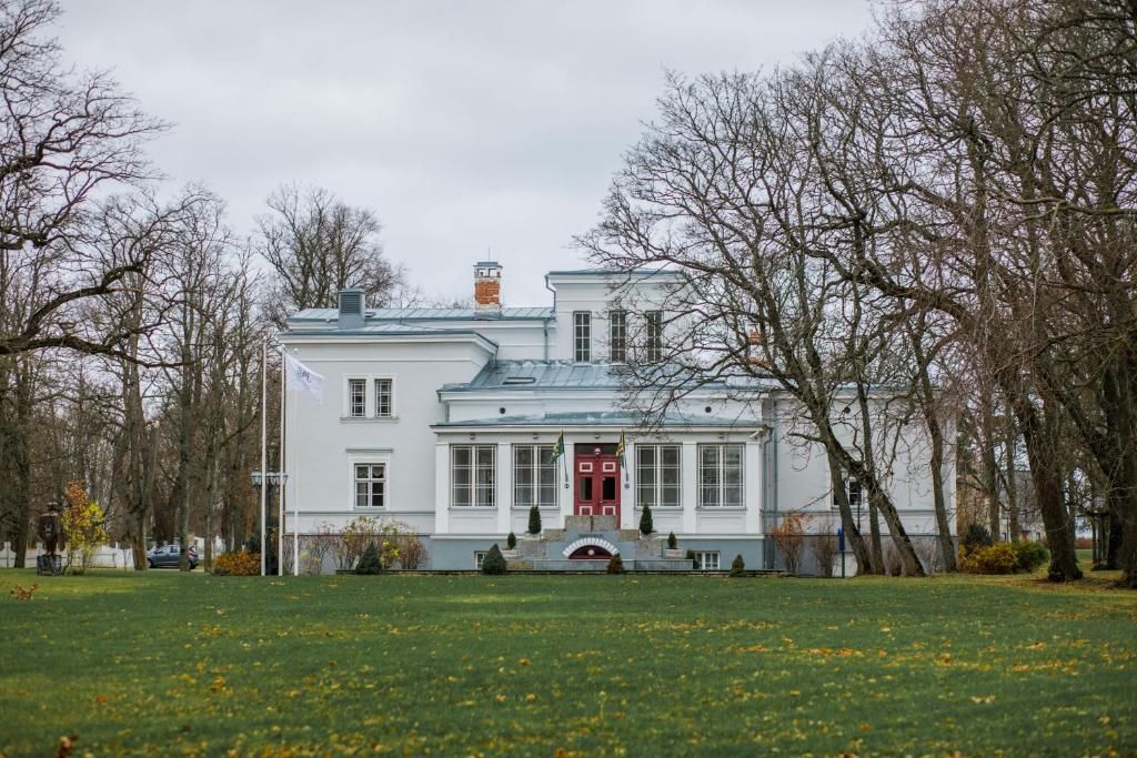 A large, white building with a red door and multiple windows, surrounded by a grassy area and leafless trees.