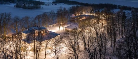 A snow-covered landscape with buildings and trees, likely a rural or countryside setting.