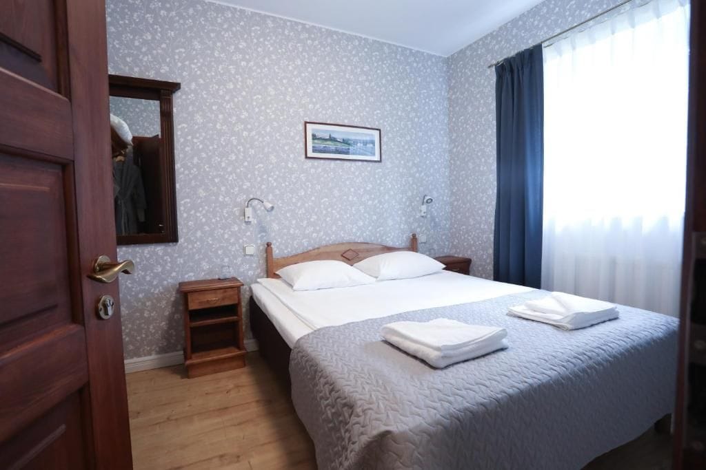 Une chambre d’hôtel avec un lit, des tables de chevet, un miroir, un tableau au mur et une fenêtre avec des rideaux.