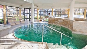 An indoor swimming pool with a stone wall, lounge chairs, and a view of the outside. - Saka Cliff Hotel & SPA (Saka)