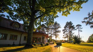 A building with a brick pathway leading to a covered entrance, surrounded by trees and a clear sky. - Saka Cliff Hotel & SPA (Saka)