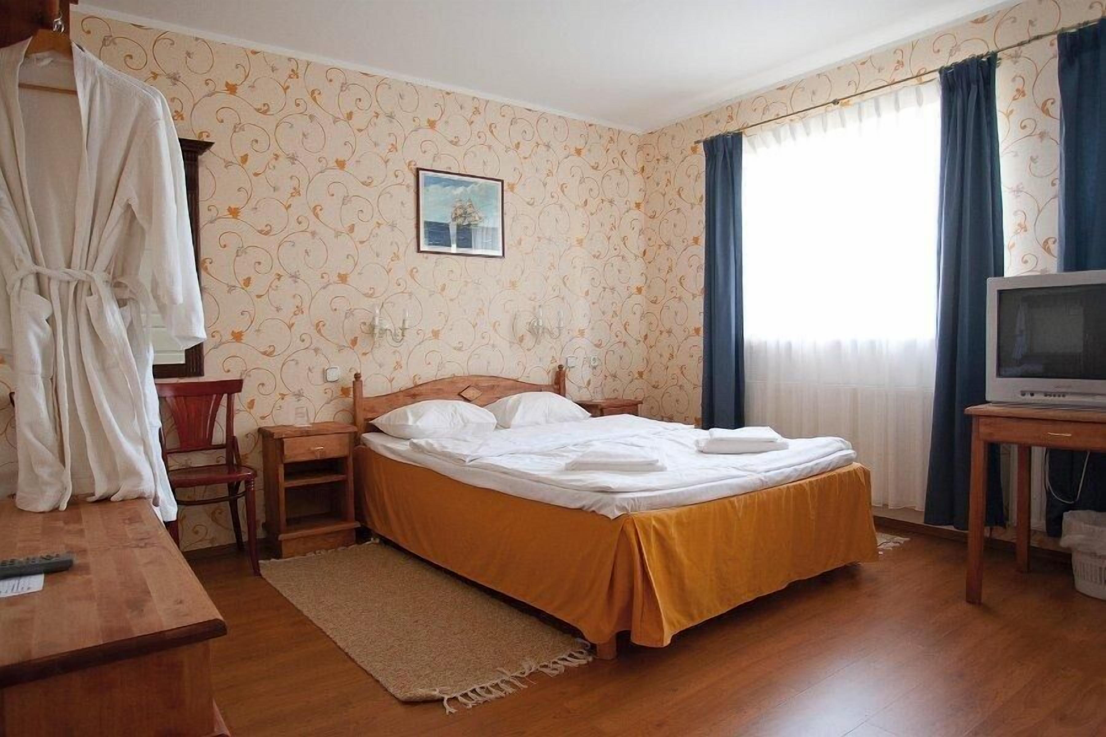A hotel room with a bed, a wooden dresser, a television, and a window with curtains.