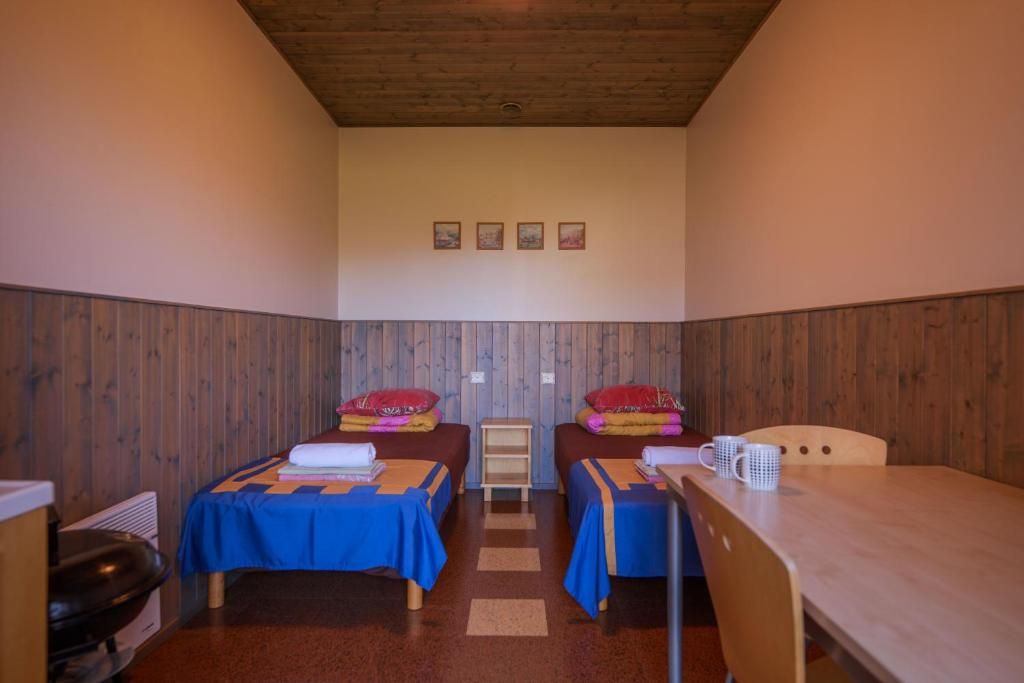 A room with two beds, a table, and a chair. There are four framed pictures on the wall.