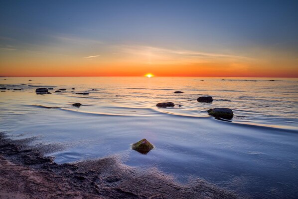 A beach scene with a sunset, calm water, and scattered rocks.