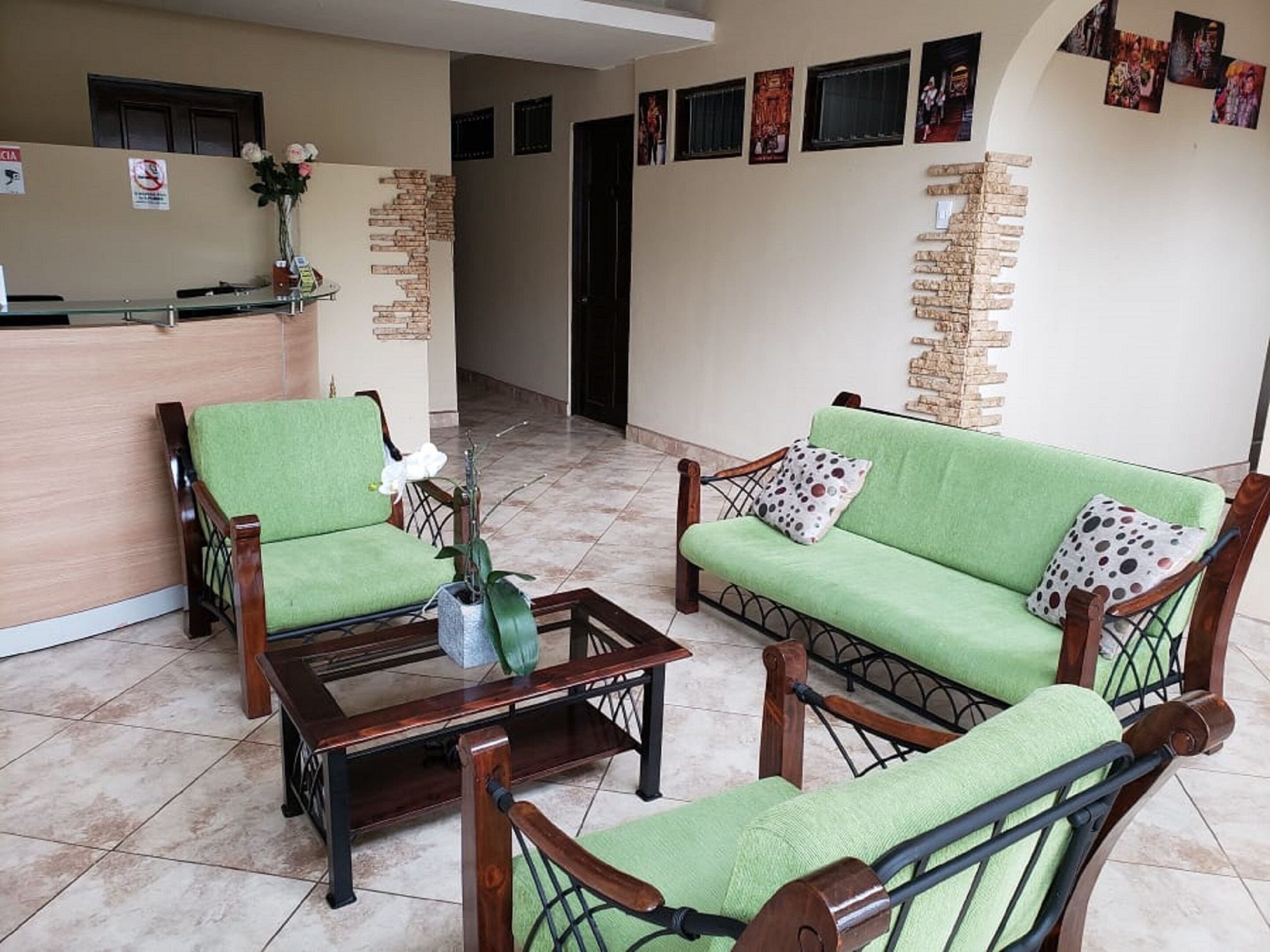 A reception area with a reception desk, two green upholstered chairs, a wooden coffee table, and a vase with flowers.