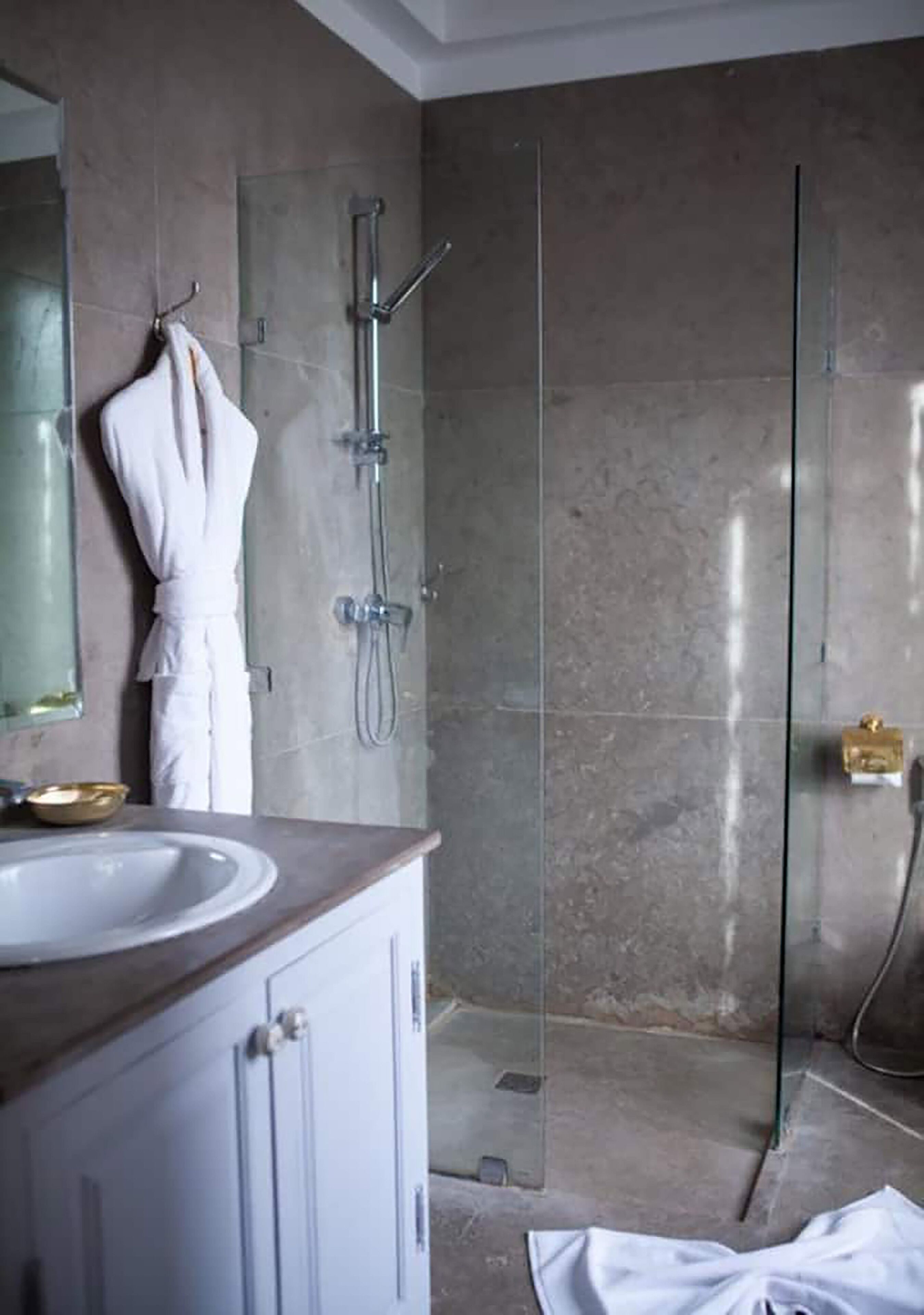 Une salle de bain moderne avec une douche à parois de verre, un peignoir blanc accroché au mur et un lavabo avec un récipient doré.