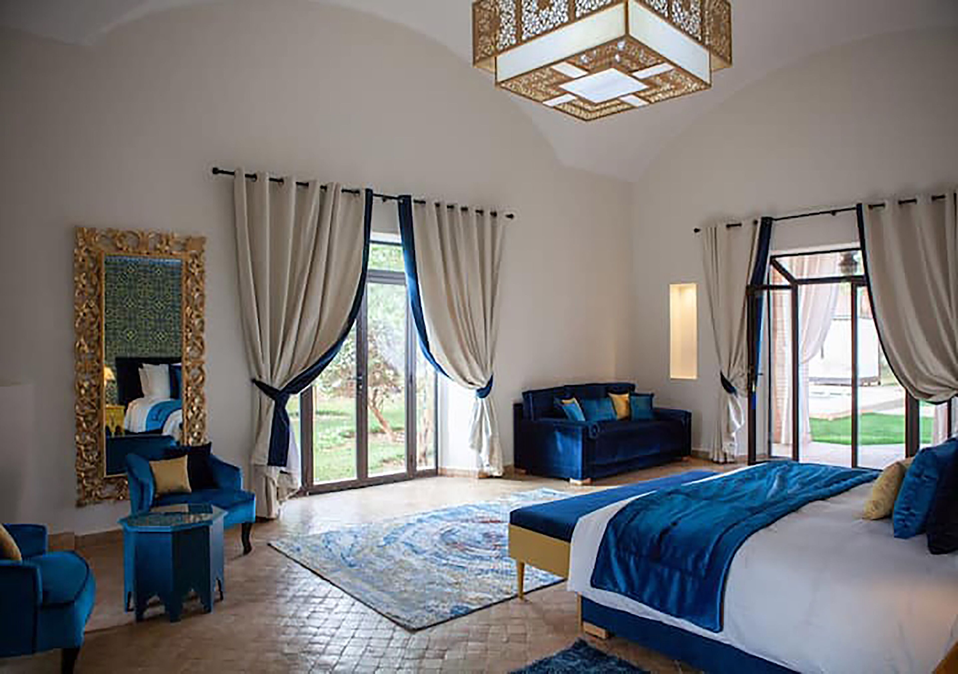 Une chambre spacieuse avec un grand lit, un canapé bleu, une petite table et une grande fenêtre avec des rideaux.