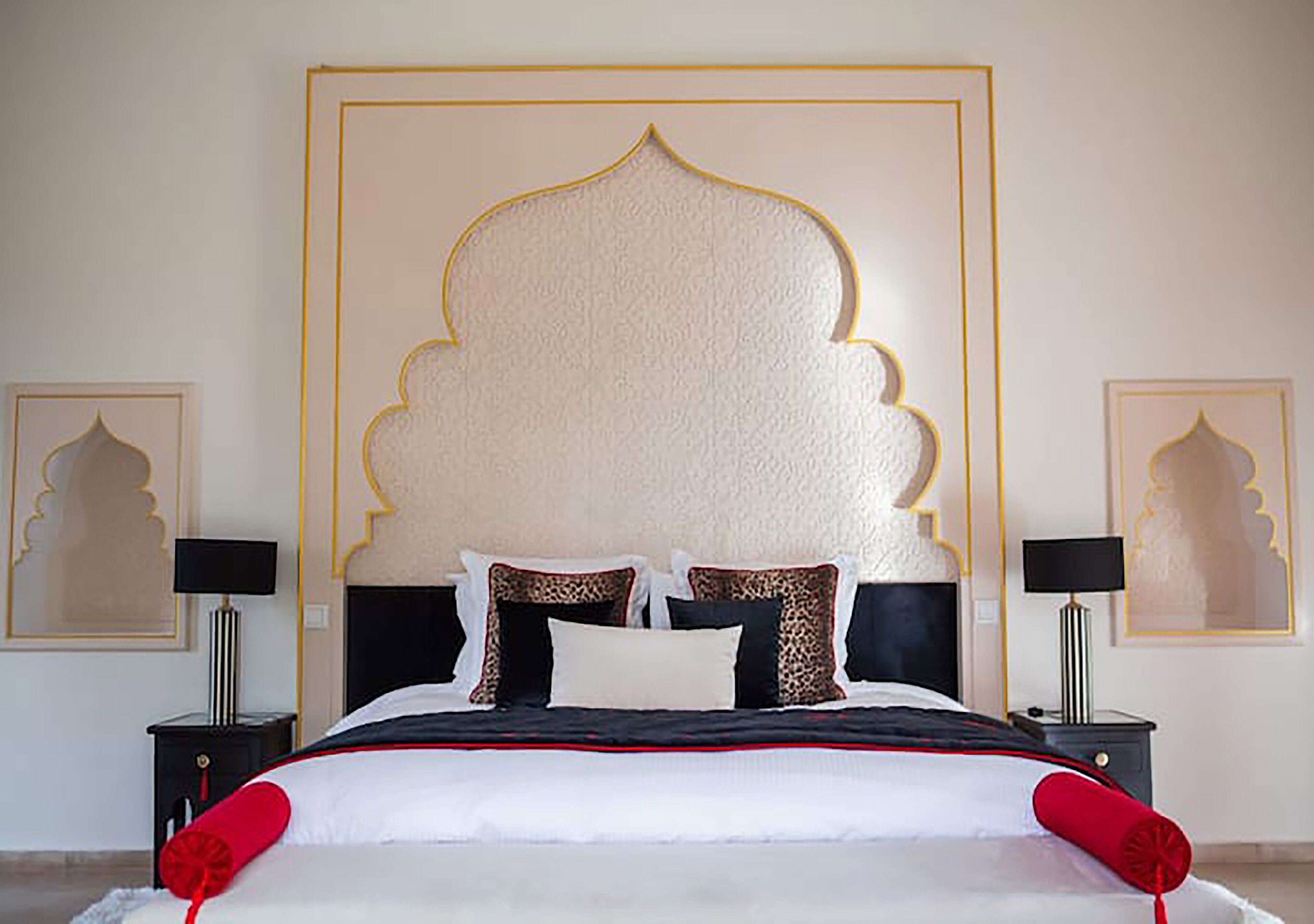 A bed with a decorative headboard, black nightstands, and framed artwork on the walls.