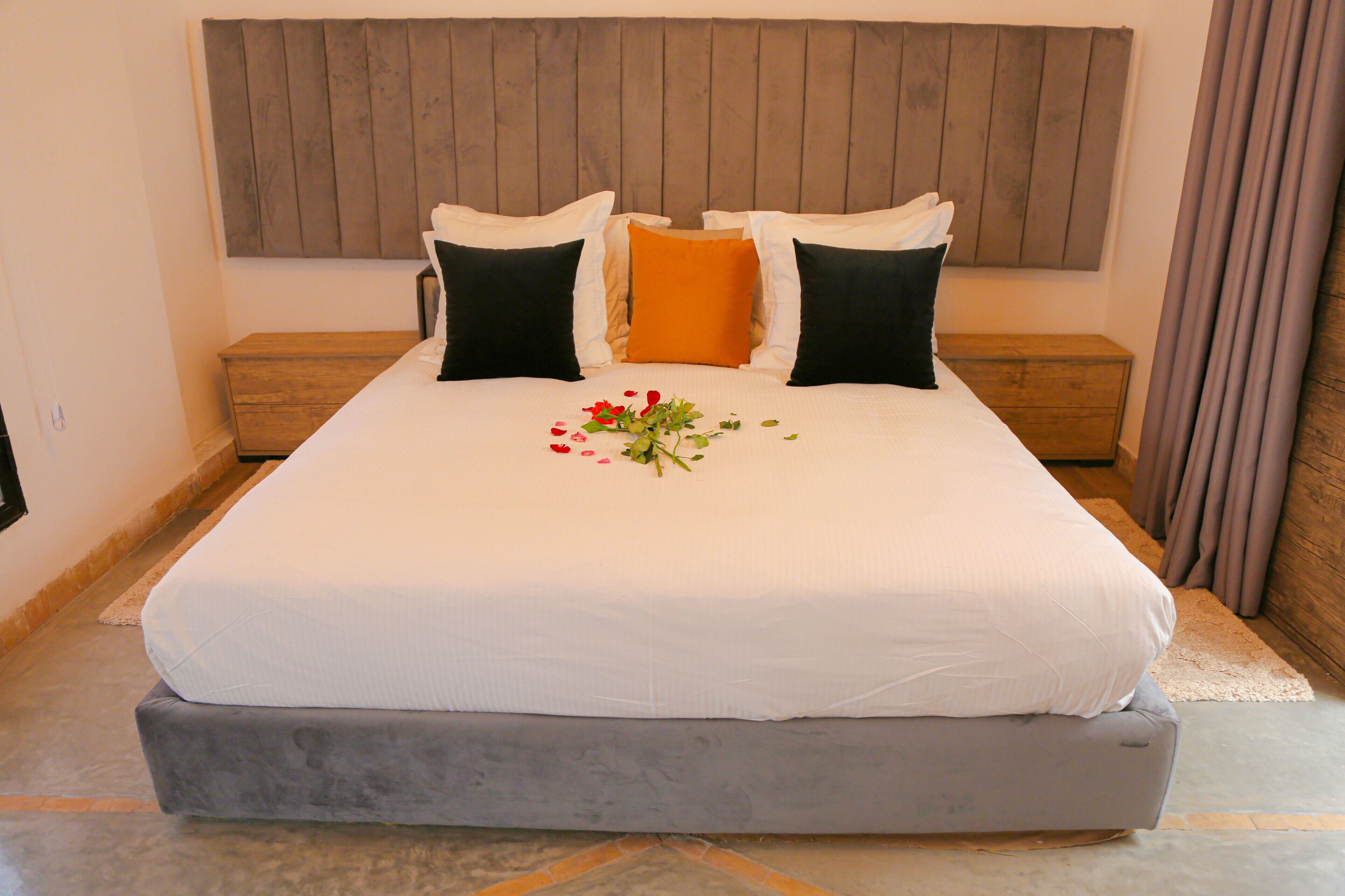 Una cama bien hecha con ropa blanca, un cabecero de madera y una única almohada naranja.