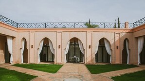 Une cour intérieure ornée d’une mosaïque centrale en forme d’étoile, entourée d’arcades en briques et de rideaux blancs.