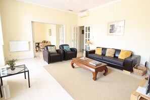 A living room with a sofa, two armchairs, a coffee table, a glass table with a plant, and a lamp.