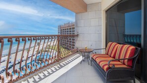 Un balcon avec vue sur la plage et la piscine, un canapé en osier et une petite table.