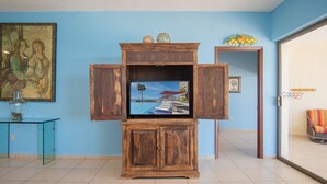 Un salon avec un meuble de rangement en bois abritant un téléviseur à écran plat, un tableau encadré et un vase posé sur une table en verre.