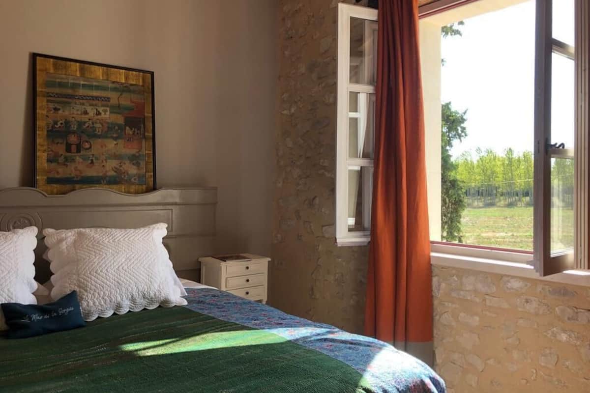 A bedroom with a bed, a nightstand, a window with curtains, and a painting on the wall.