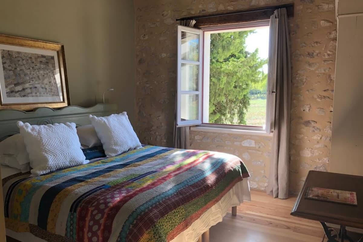 A bedroom with a bed, a window, a table, and a framed picture on the wall.