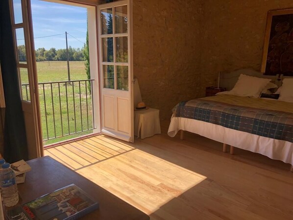 Un dormitorio con una cama, una mesita con una botella de agua, una silla y vistas a un campo verde a través de una puerta de vidrio.