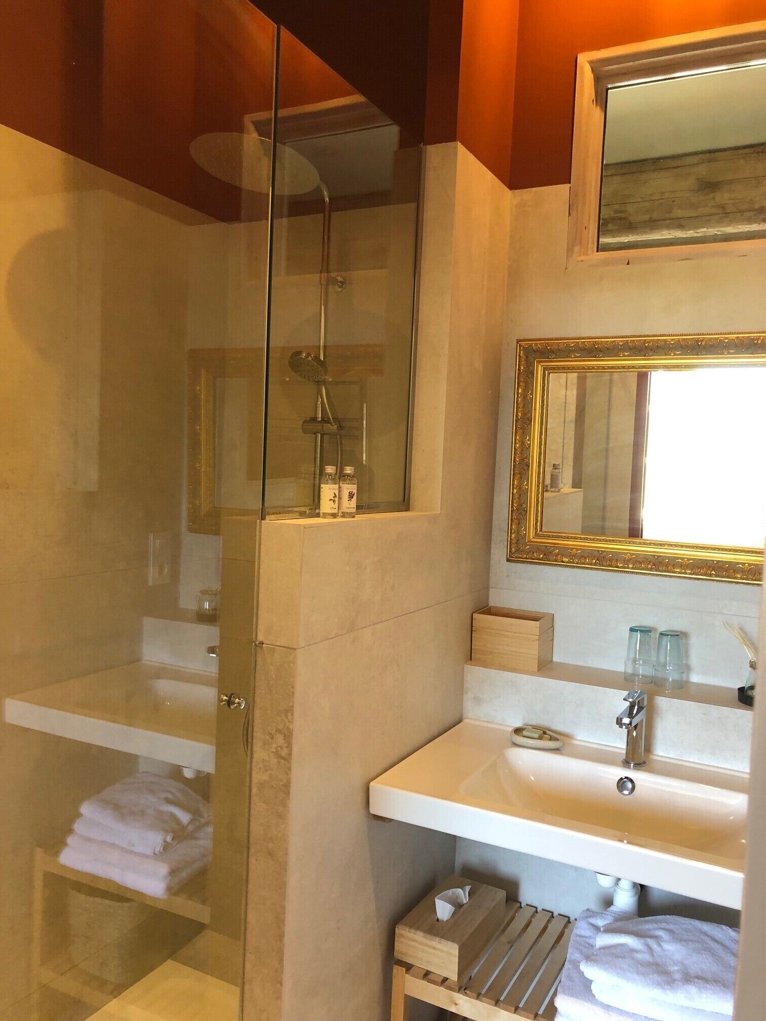 A modern bathroom with a glass-enclosed shower, a white sink, and a mirror with a gold frame.