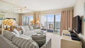 Un salon moderne avec un canapé, une table basse et un téléviseur, un balcon avec des rideaux et une grande fenêtre.