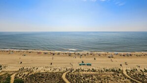 Une plage avec des tentes et des parasols, un sentier sablonneux et une clôture.