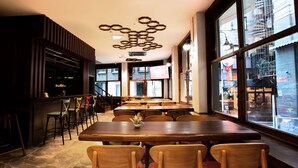 A restaurant with a bar area, multiple tables and chairs, and large windows offering a view of the street. - West Palace Hotel (Istanbul)