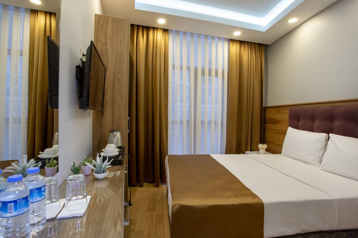 A hotel room with a bed, a desk with water bottles, a mirror, and curtains.